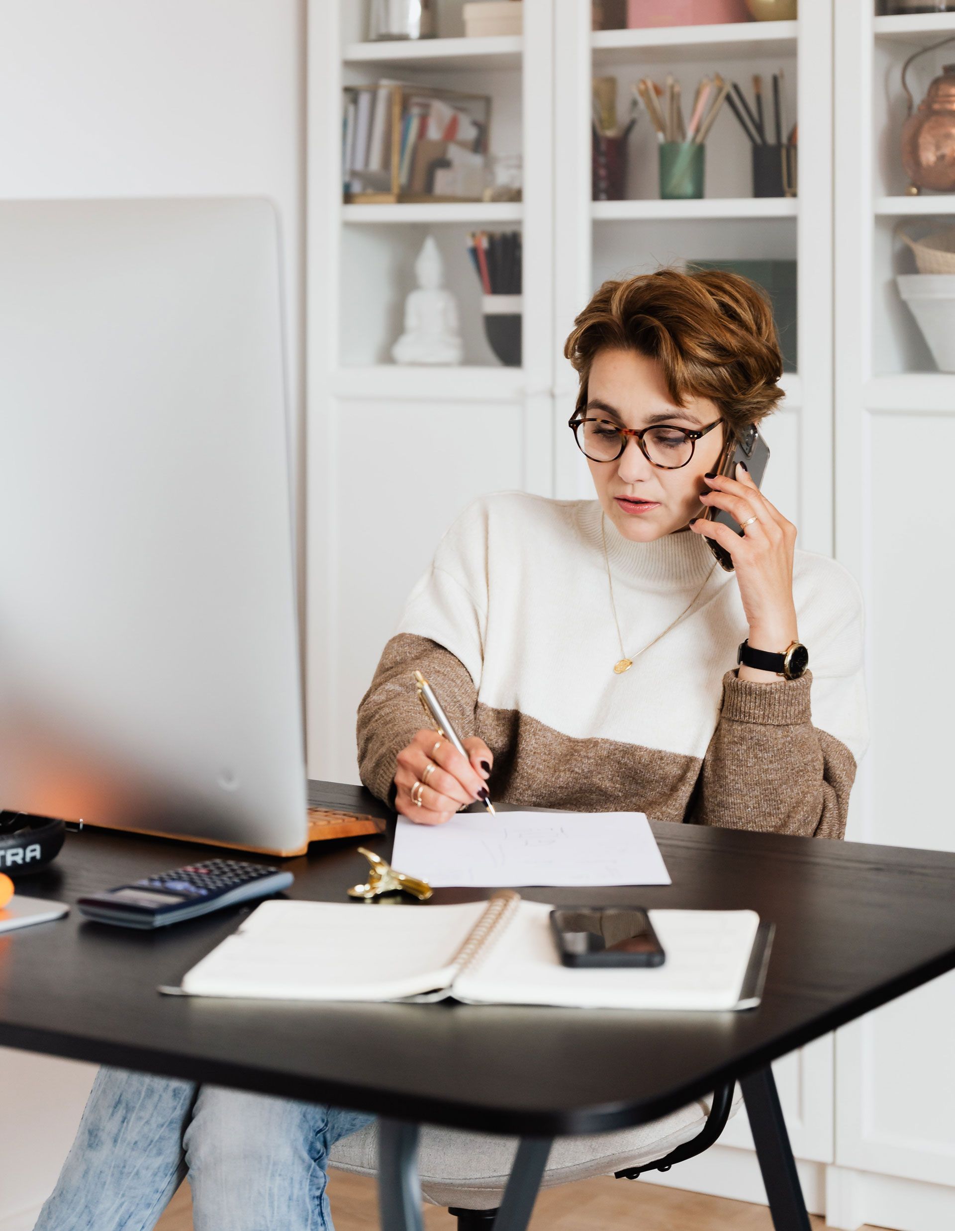 A woman is sitting at a desk talking on a cell phone.