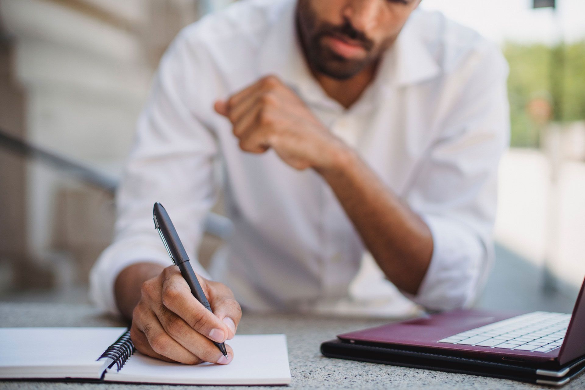 A man is sitting at a table writing in a notebook.