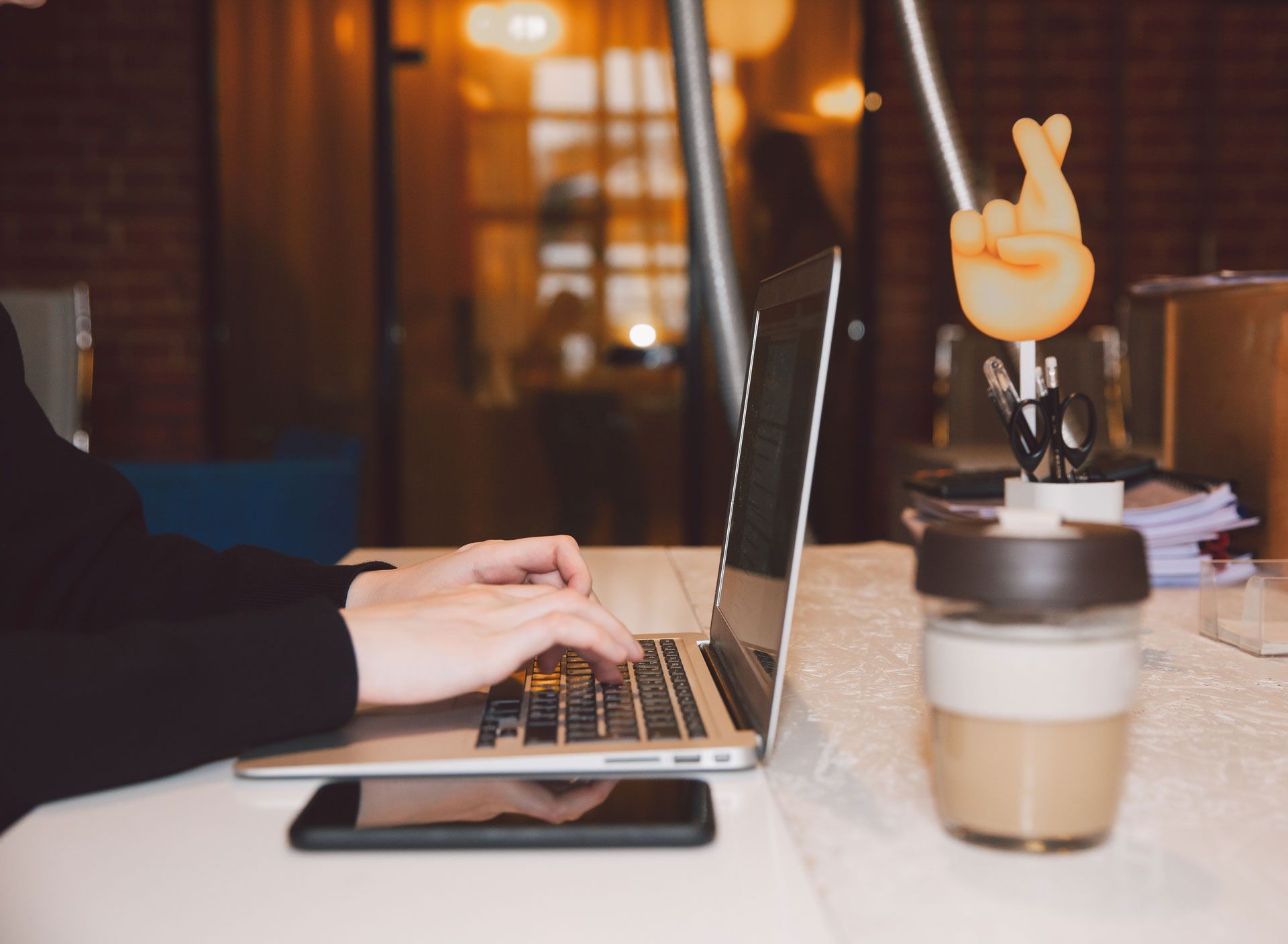 A person is typing on a laptop next to a cup of coffee.