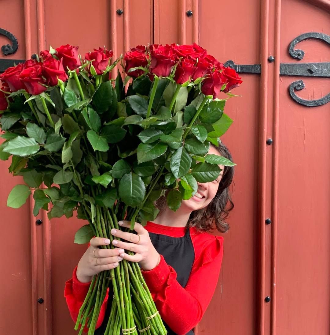 a woman is holding a large bouquet of red roses in front of her face .