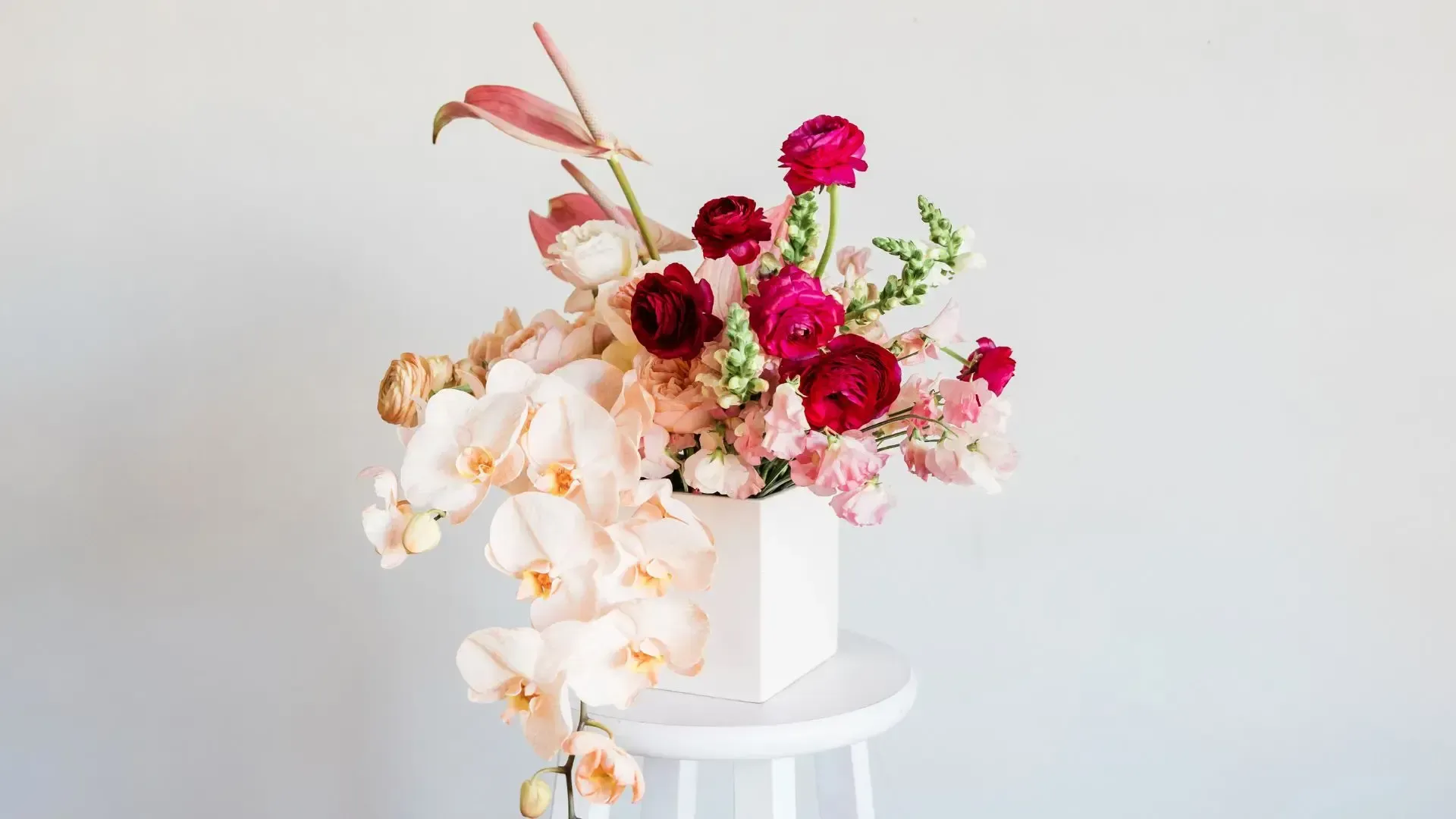 A vase filled with pink and red flowers is sitting on a white table.