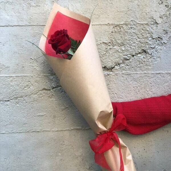 a single red rose wrapped in brown paper with a red bow