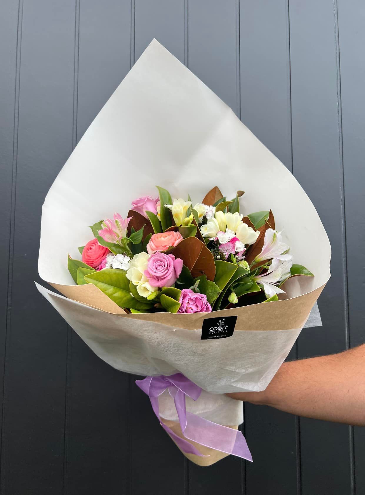 a person is holding a bouquet of flowers wrapped in white paper .