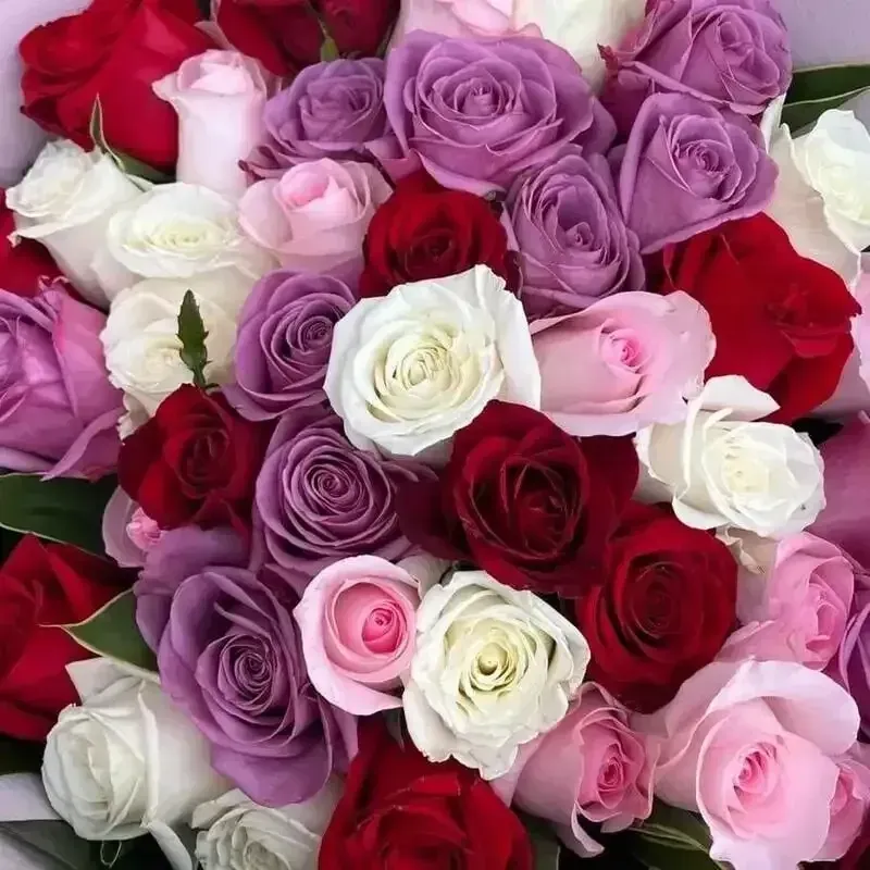 Christmas wreath with red roses, white flowers, and green foliage against a white brick wall.