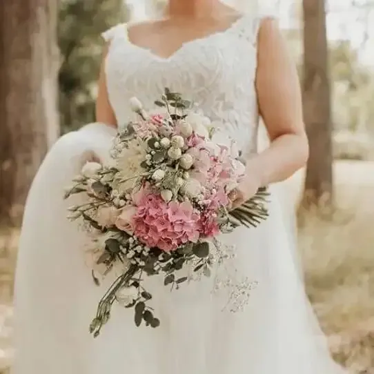 a bride in a white dress is holding a bouquet of pink and white flowers .