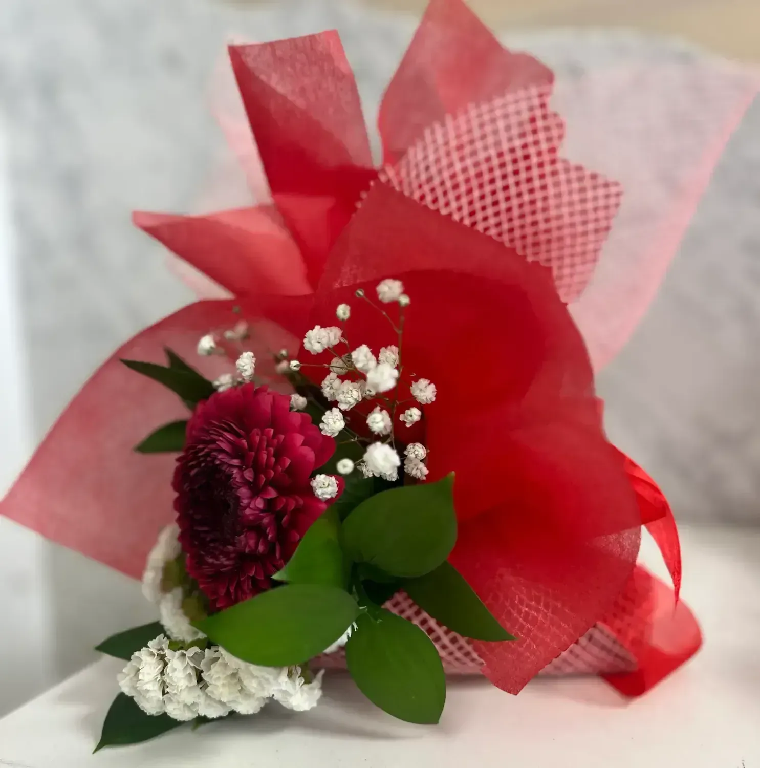 Red and white floral arrangement wrapped in red tissue paper.