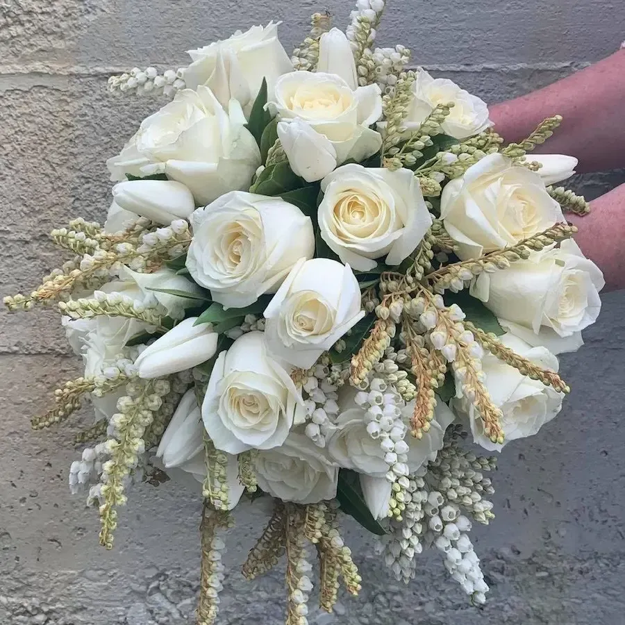 a person is holding a bouquet of white roses and yellow flowers .