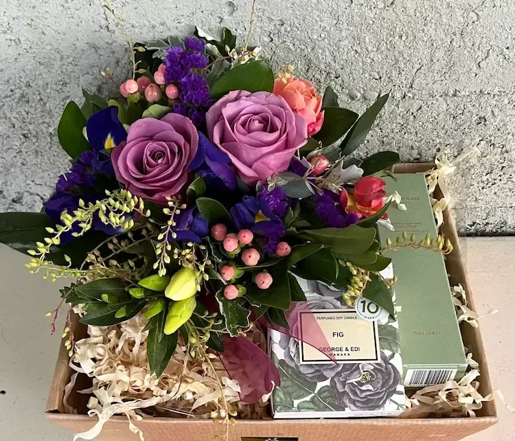 Arrangement of purple and pink flowers with gifts in a box.