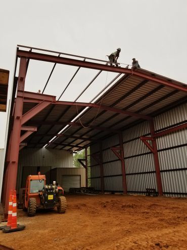 Construction of a red metal building with workers on the roof