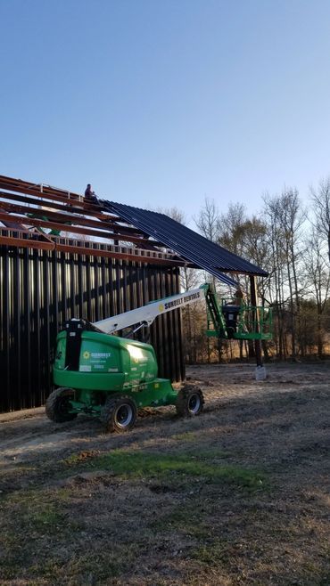 Green lift assisting construction of black metal building with exposed wooden roof framing