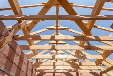 Wooden roof structure under construction against a blue sky