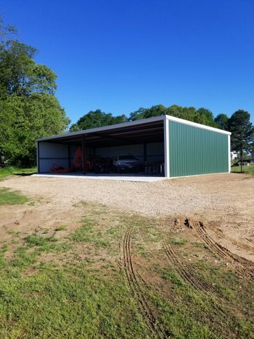 Green and silver metal shed with open side, gravel ground, blue sky