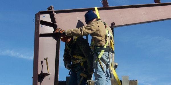 Two construction workers wearing safety harnesses on steel frame