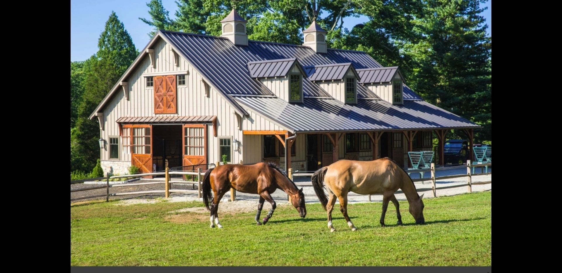 Two horses graze in a grassy field in front of a barn-style house