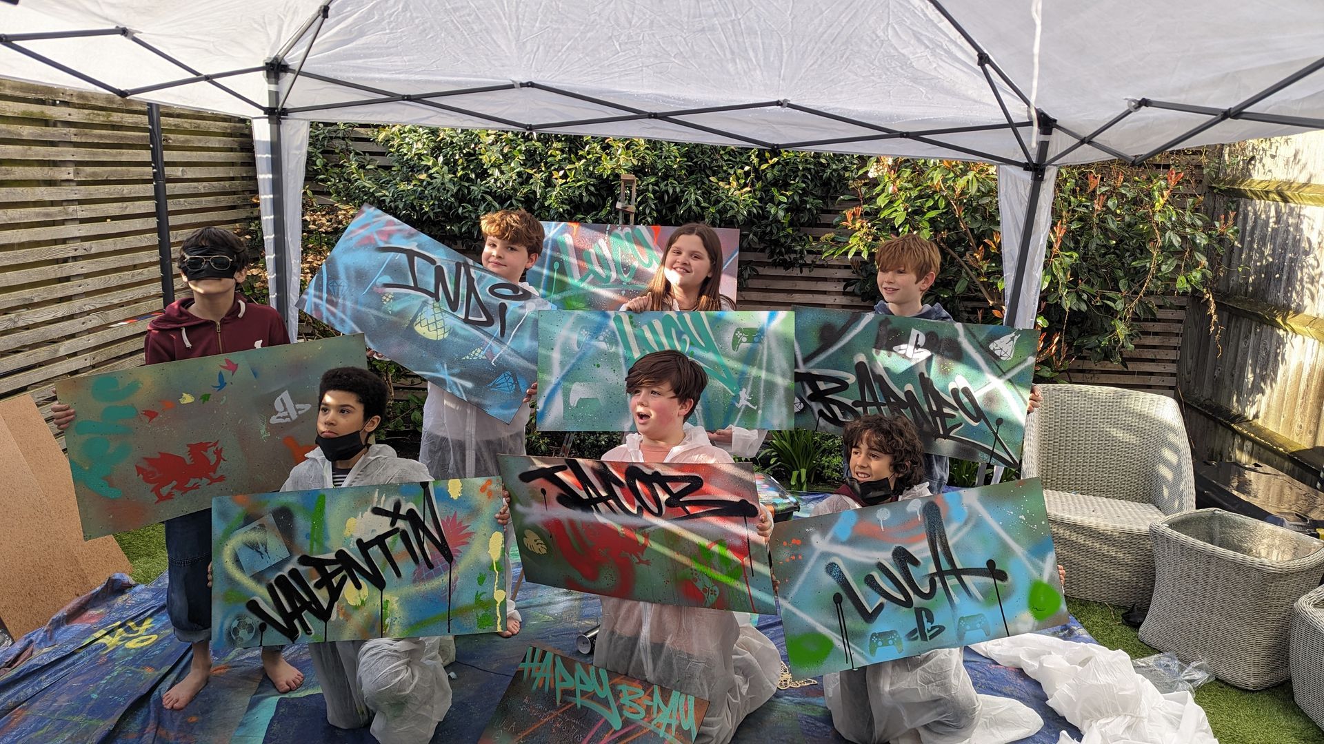 Outdoor home graffiti party setup with children spray painting boards in a garden at a Street Stars birthday event.
