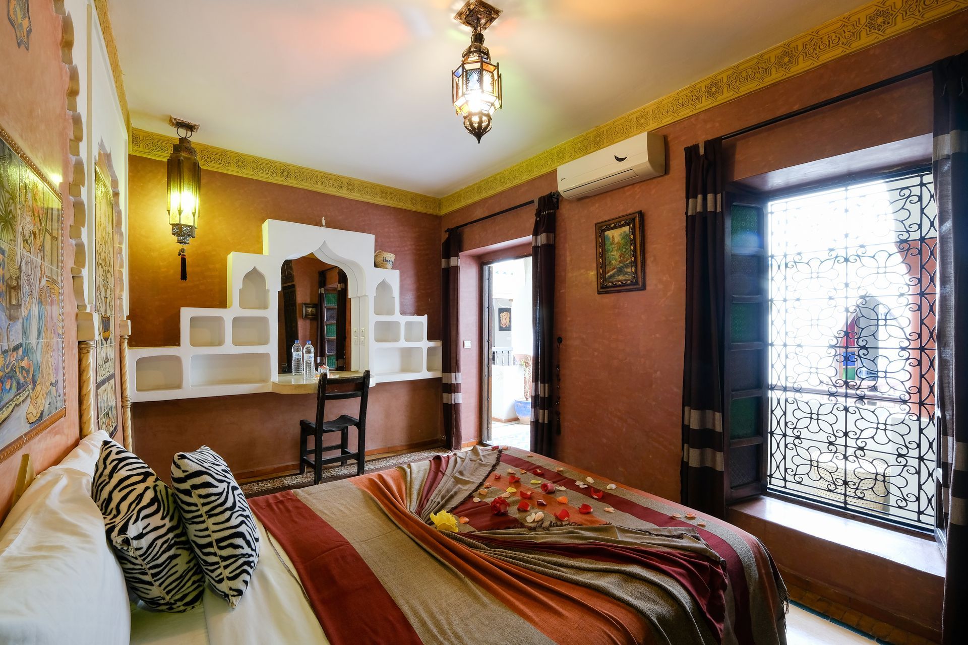 Bedroom with Moroccan decor: orange walls, arched alcove with shelves, patterned bedding, window with ornate grill.