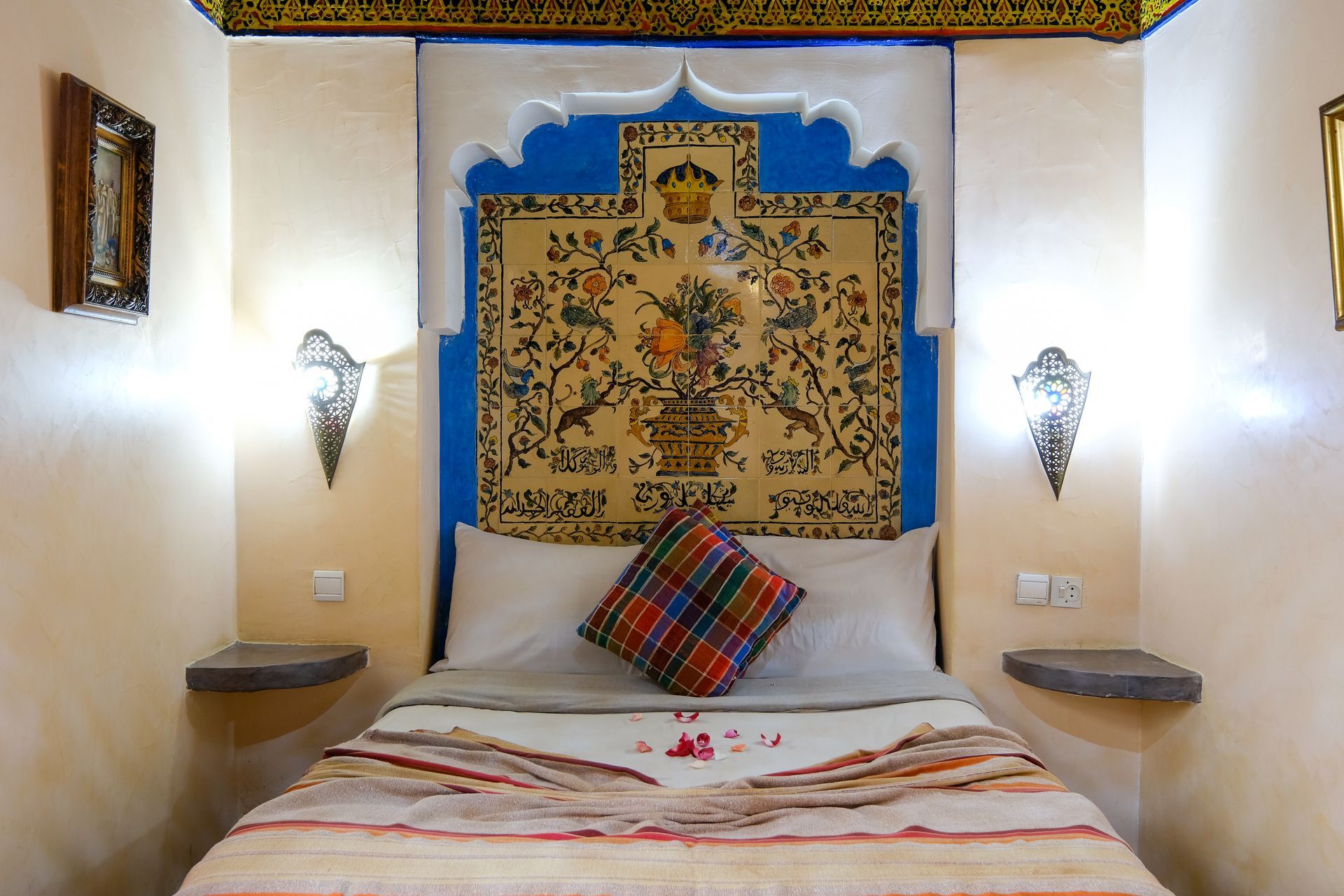 Bedroom with blue and white arched headboard, decorative tapestry, and bedside sconces.
