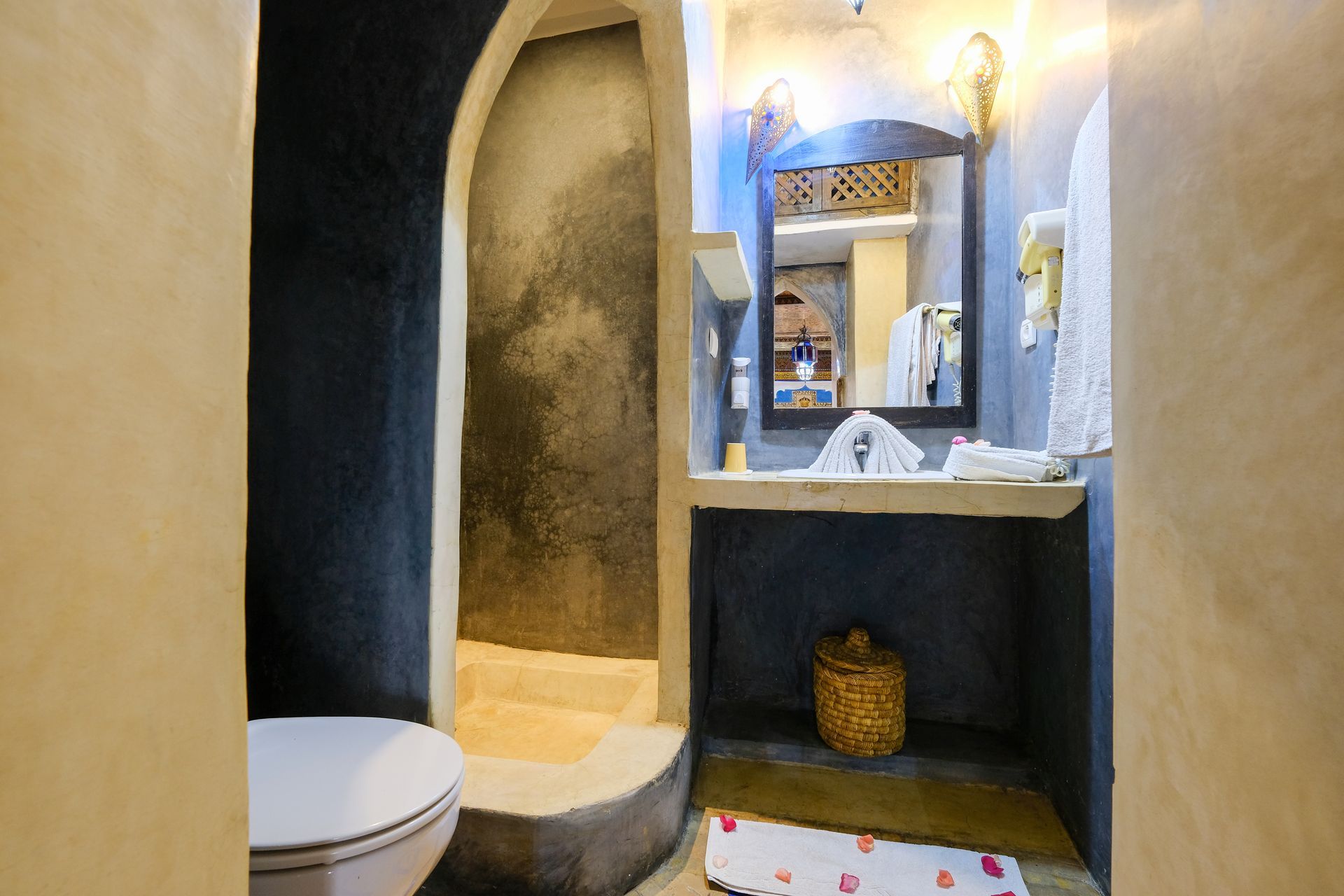 Bathroom with dark blue walls, curved doorways, white sink, toilet, and woven basket.