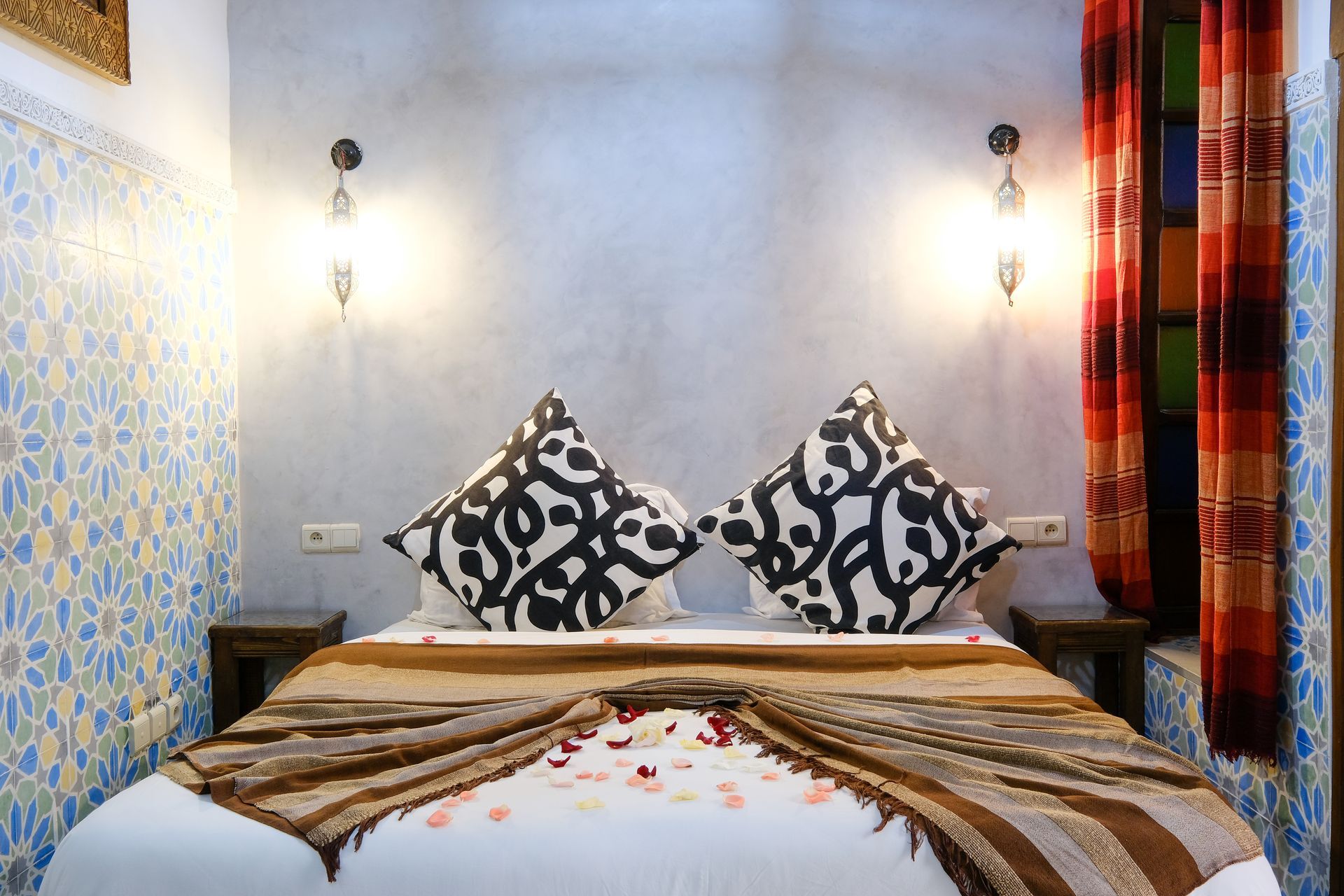 Bedroom with a bed, patterned pillows, decorative bedspread, and colorful stained-glass window.