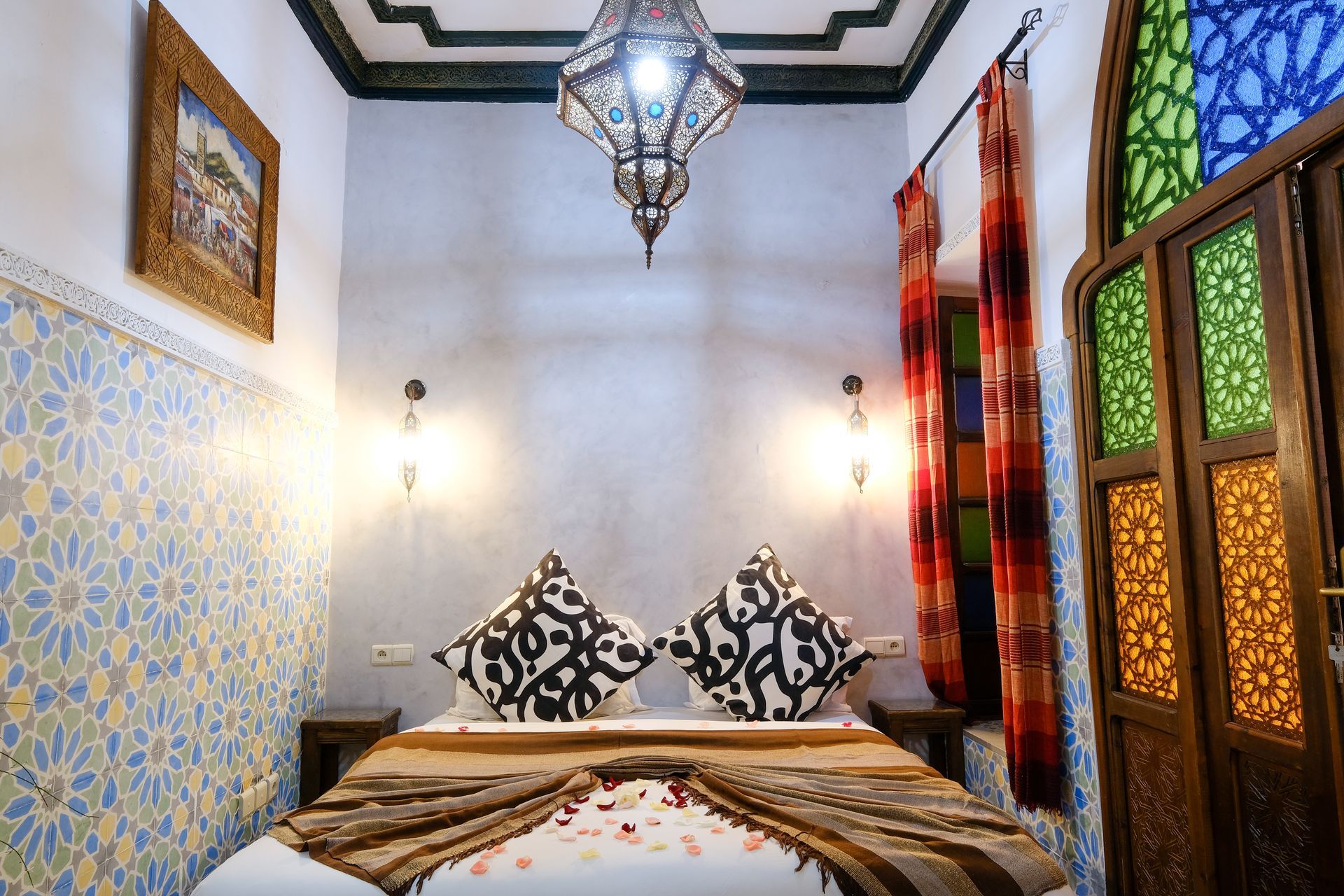 Bedroom with ornate details: bed, patterned pillows, hanging lantern, stained-glass window.
