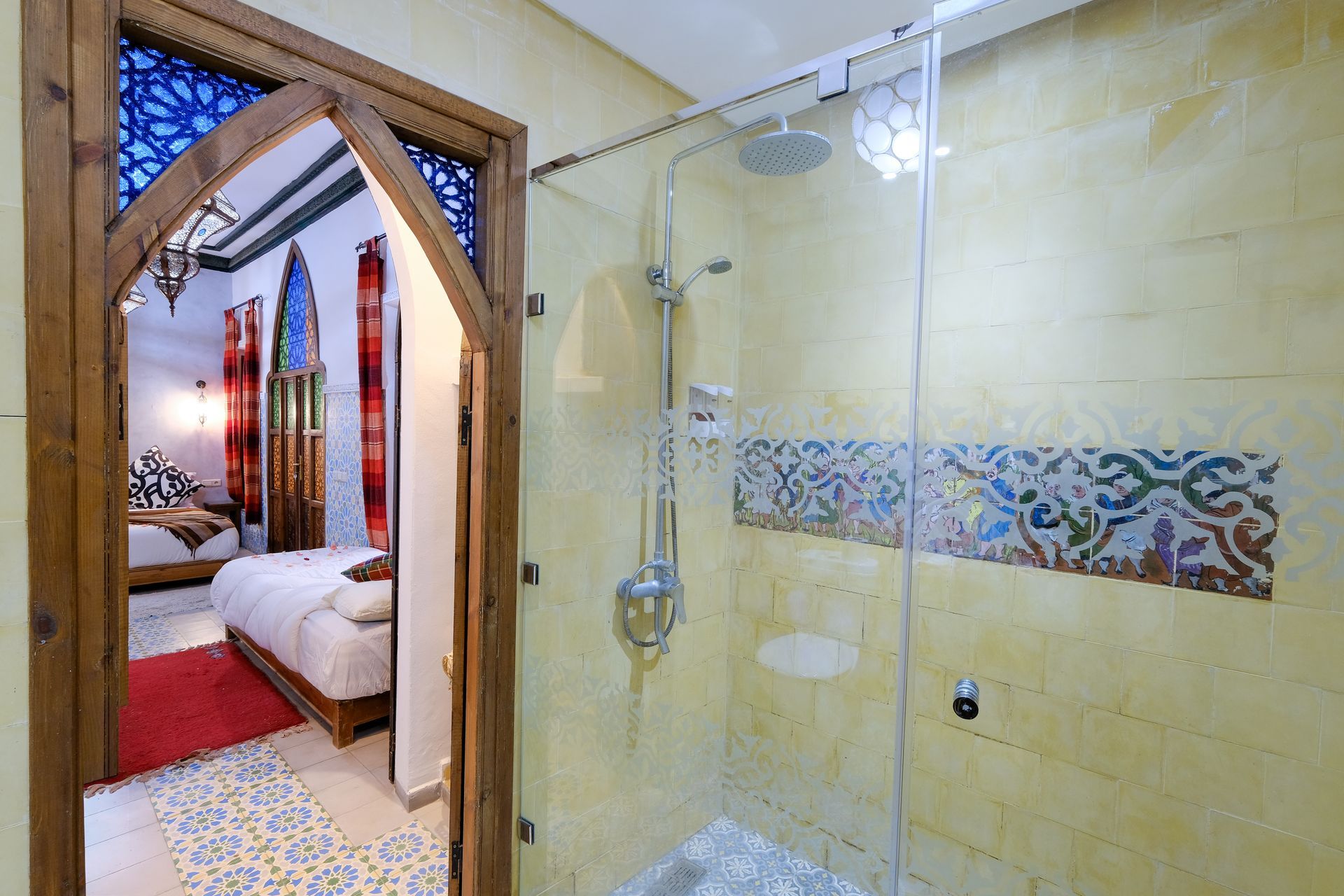 Bathroom with glass shower, patterned tile accent, and doorway to bedroom with bed.