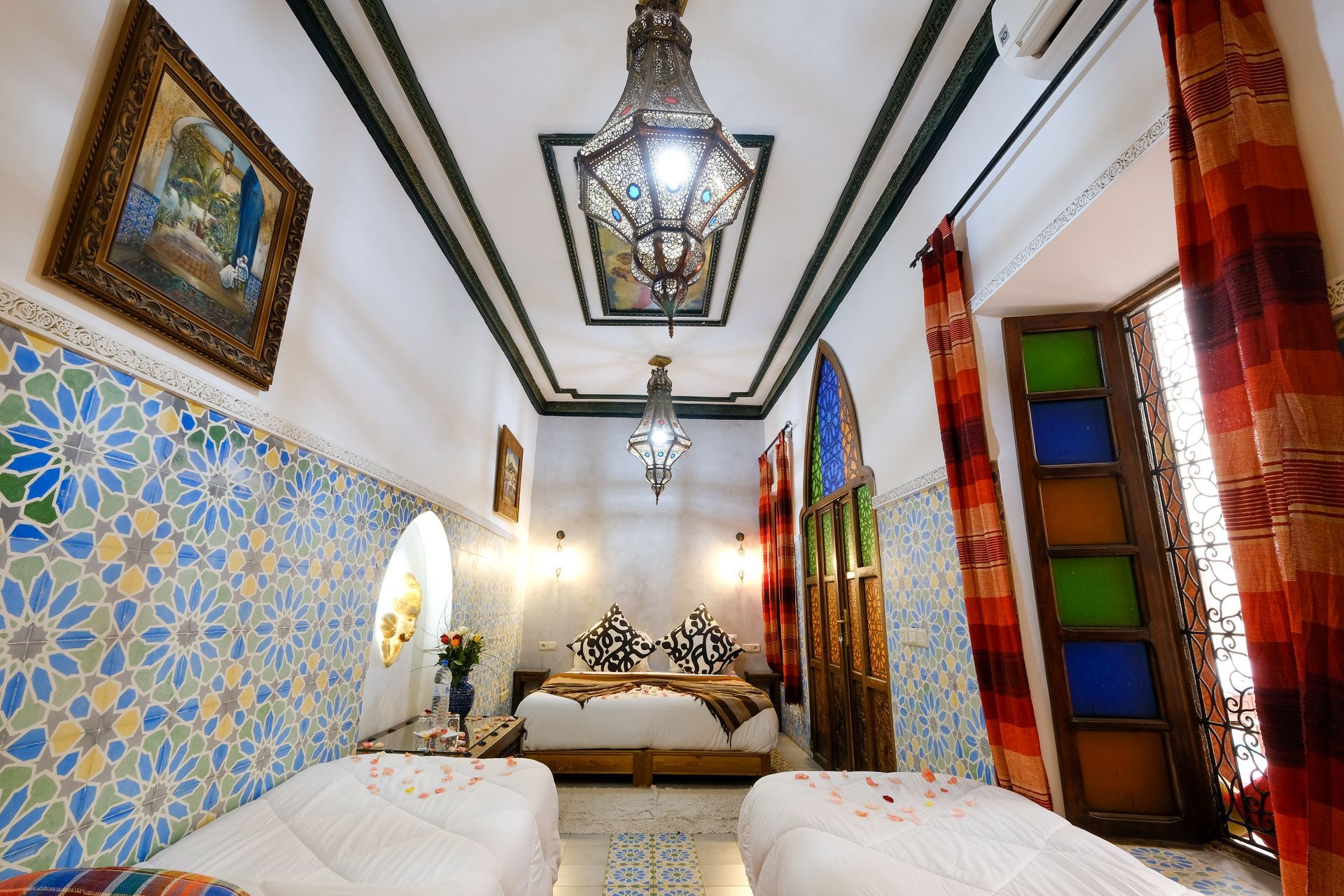 Moroccan-style bedroom with blue and white tile, ornate lanterns, and colorful stained-glass window.