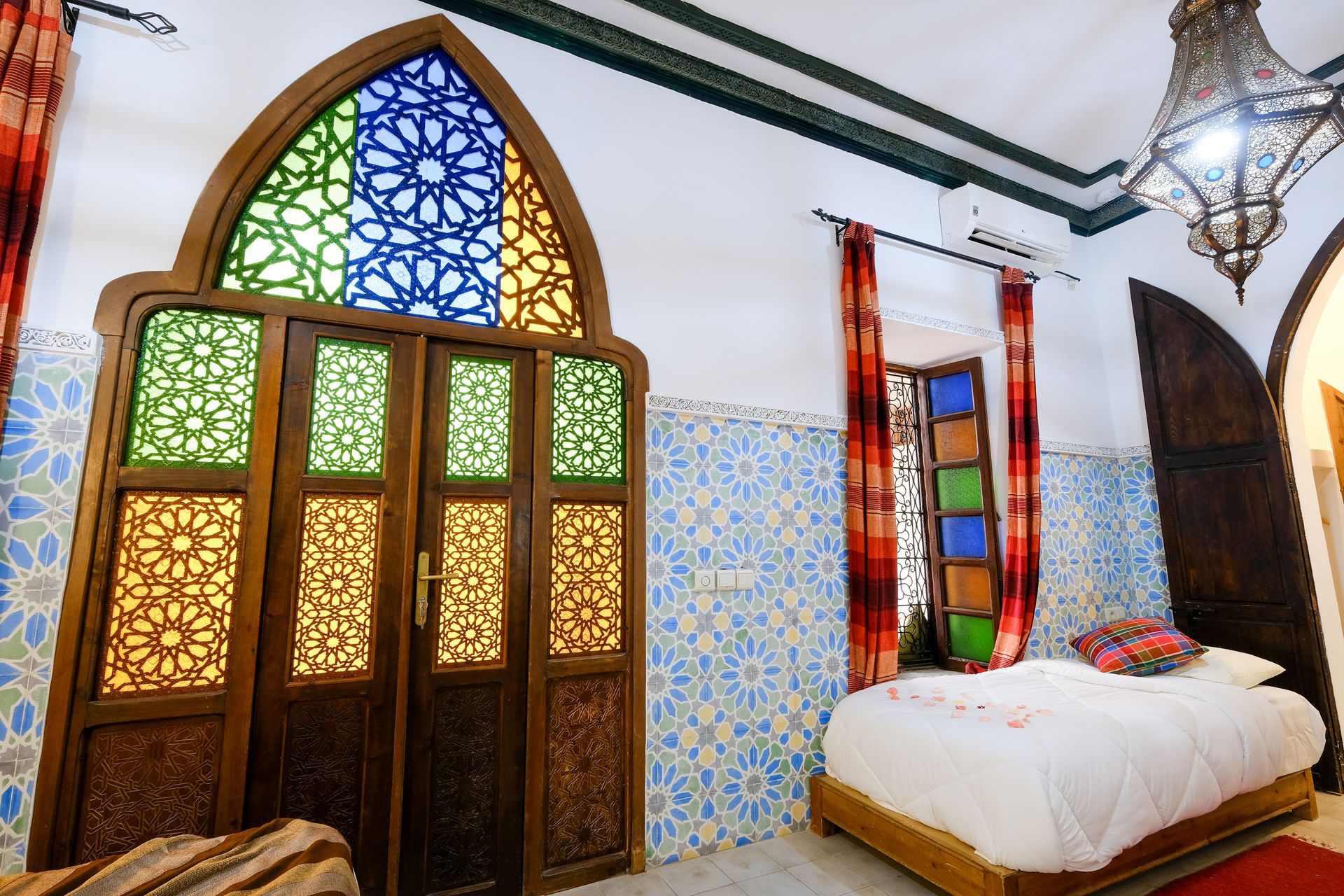 Moroccan-style bedroom with stained glass doors and windows, light blue tile, and ornate wooden bed.