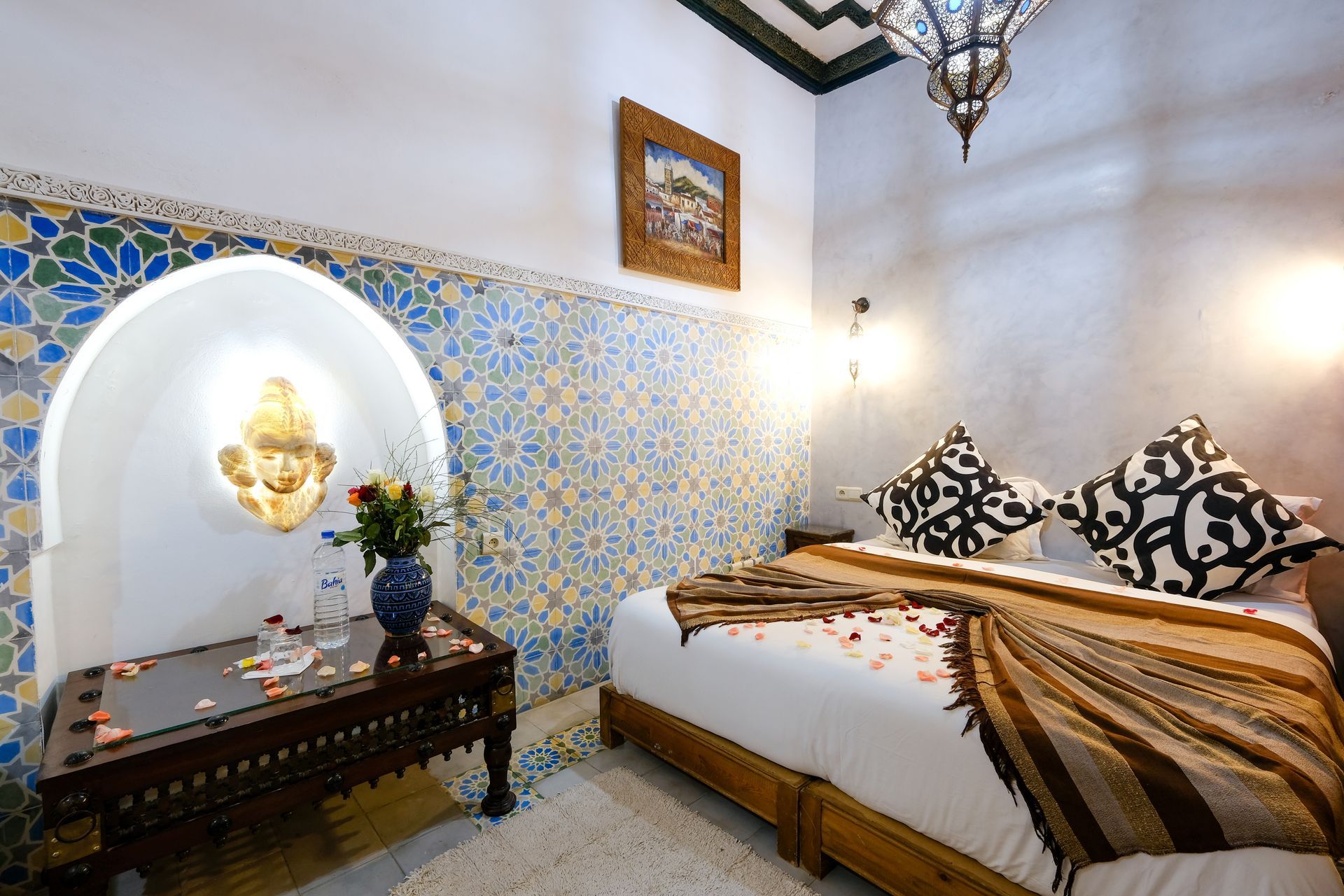 Bedroom with a Moroccan design, features tiled walls, a wooden table, and a bed with decorative pillows and blanket.