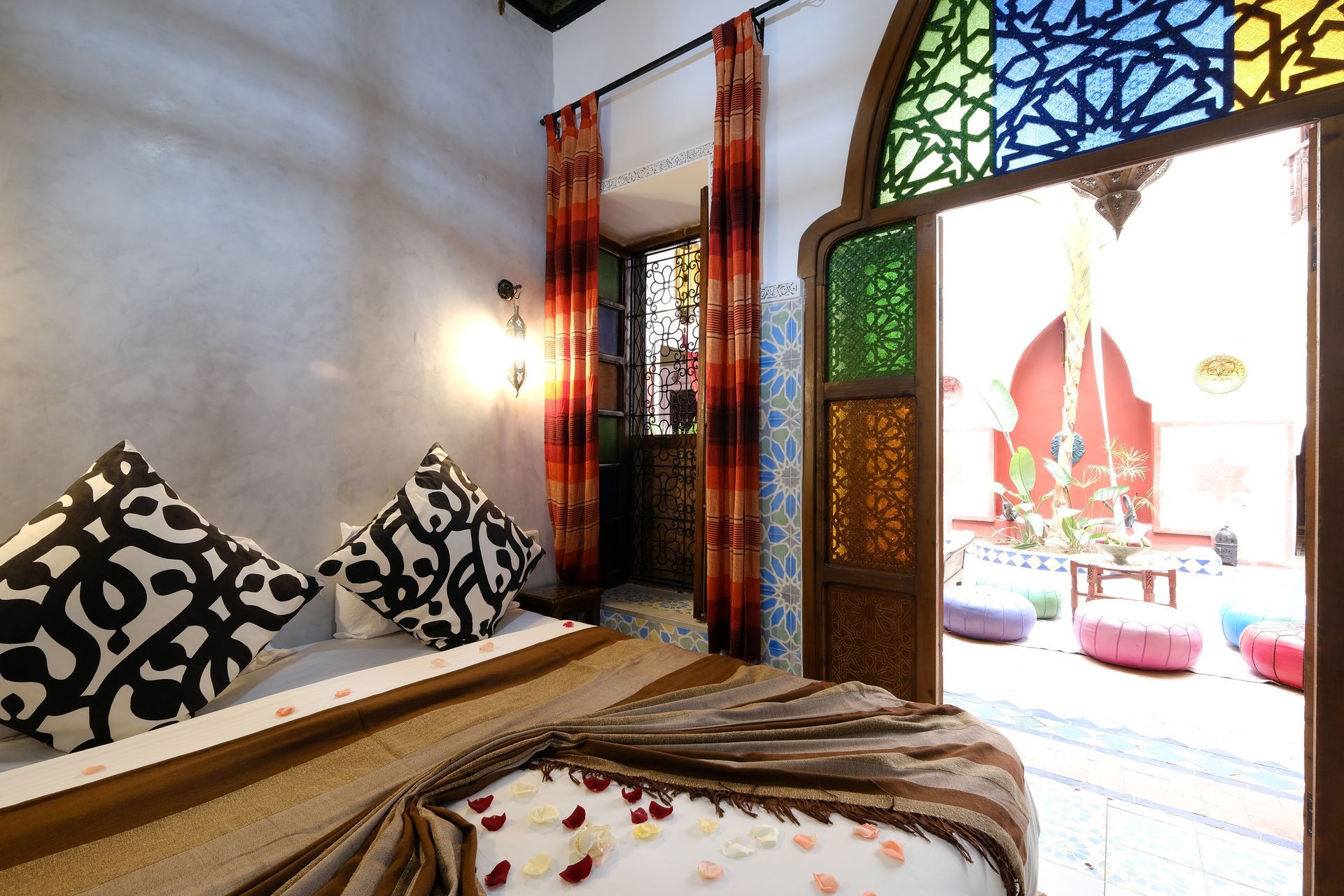 Bedroom doorway to courtyard, stained glass, patterned pillows, rose petals, colorful poufs.