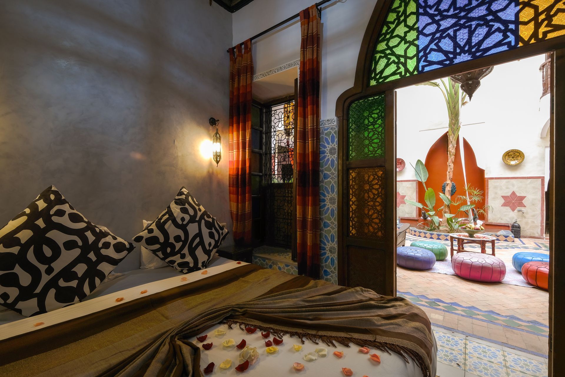 Bedroom with view to courtyard; bed with patterned pillows, colorful doorway, and outdoor seating.