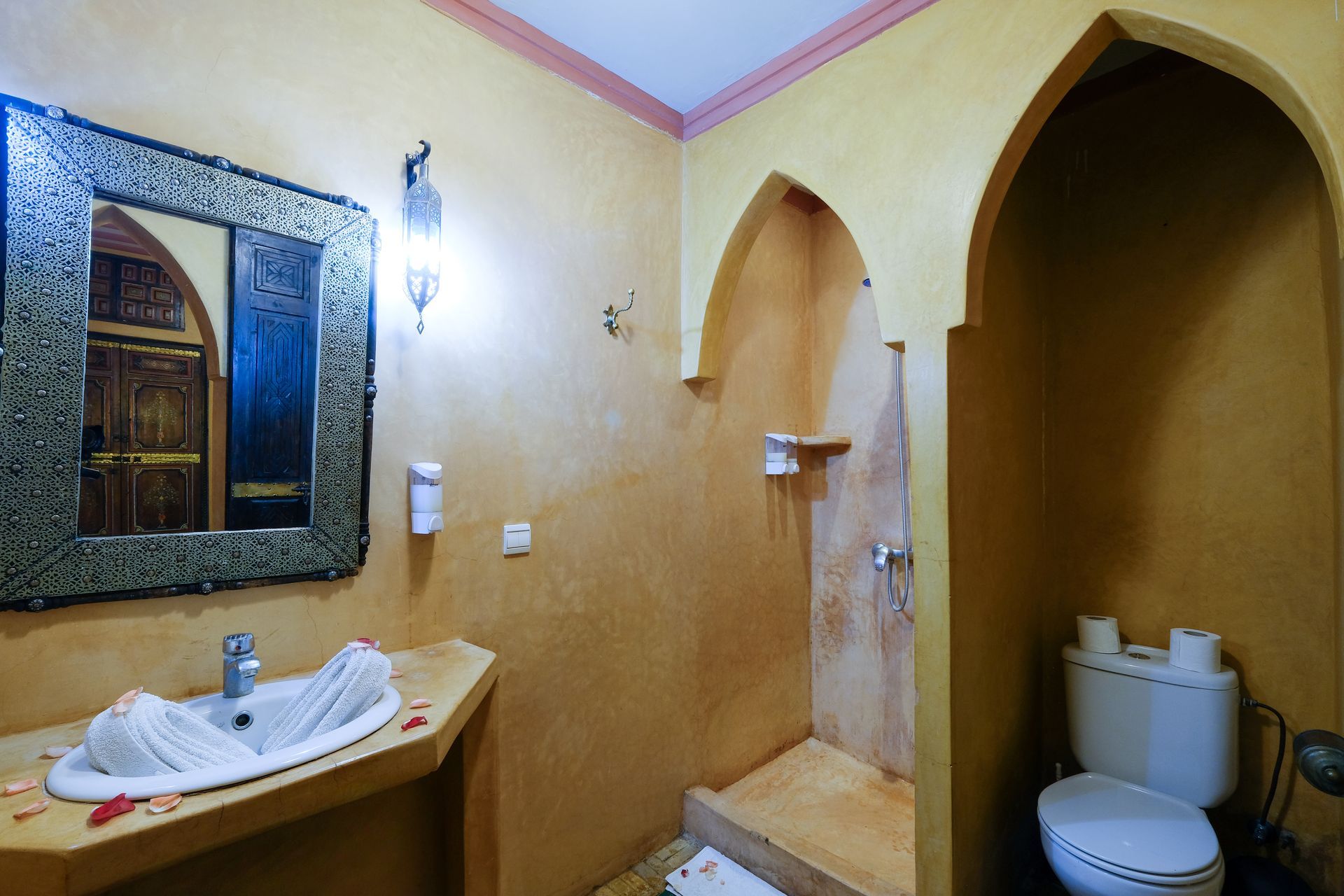 Bathroom with arched doorways, ornate mirror, sink, toilet, and a walk-in shower. Yellow walls.