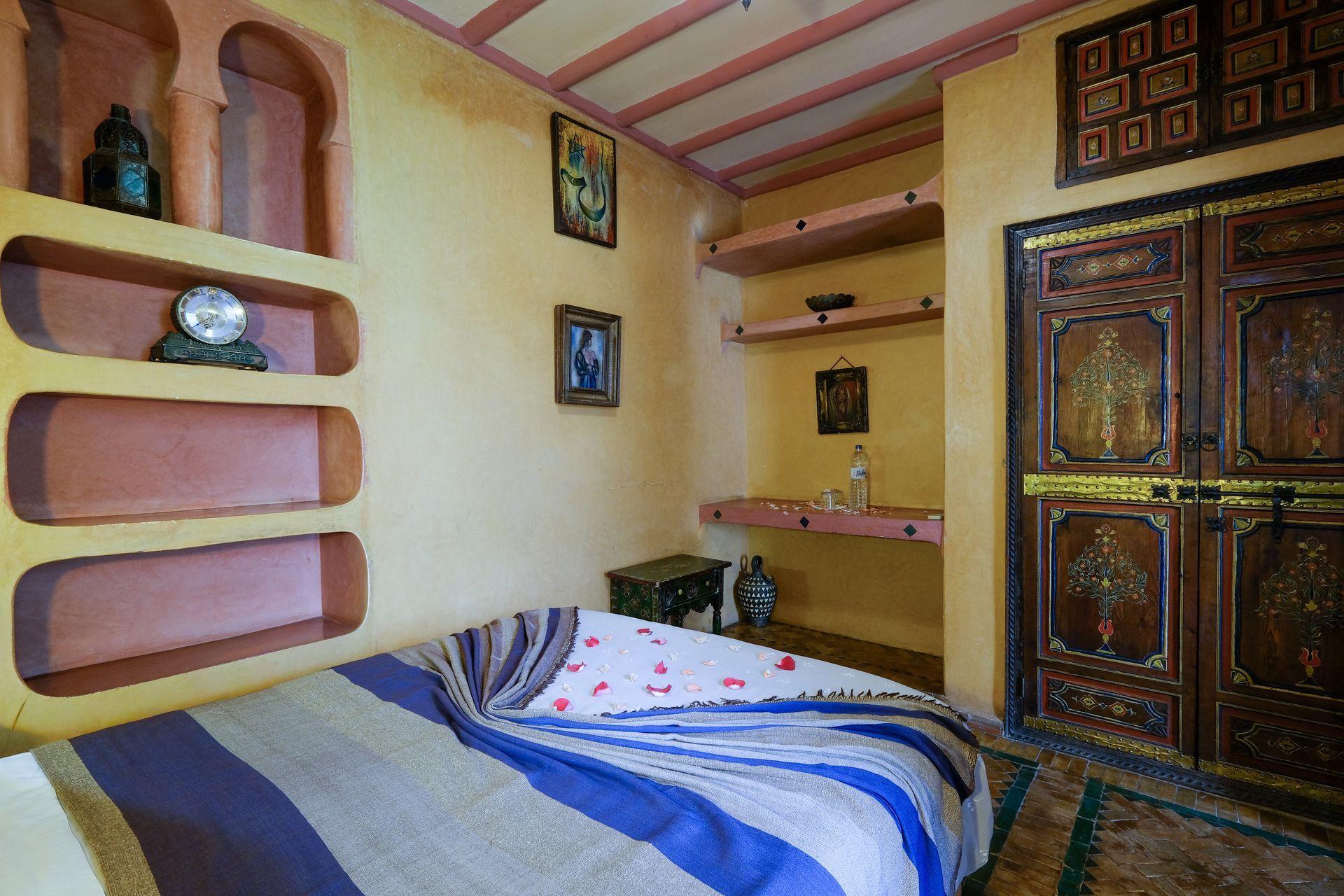 Bedroom with arched shelves, a bed with blue and white blanket, and ornate wooden doors.