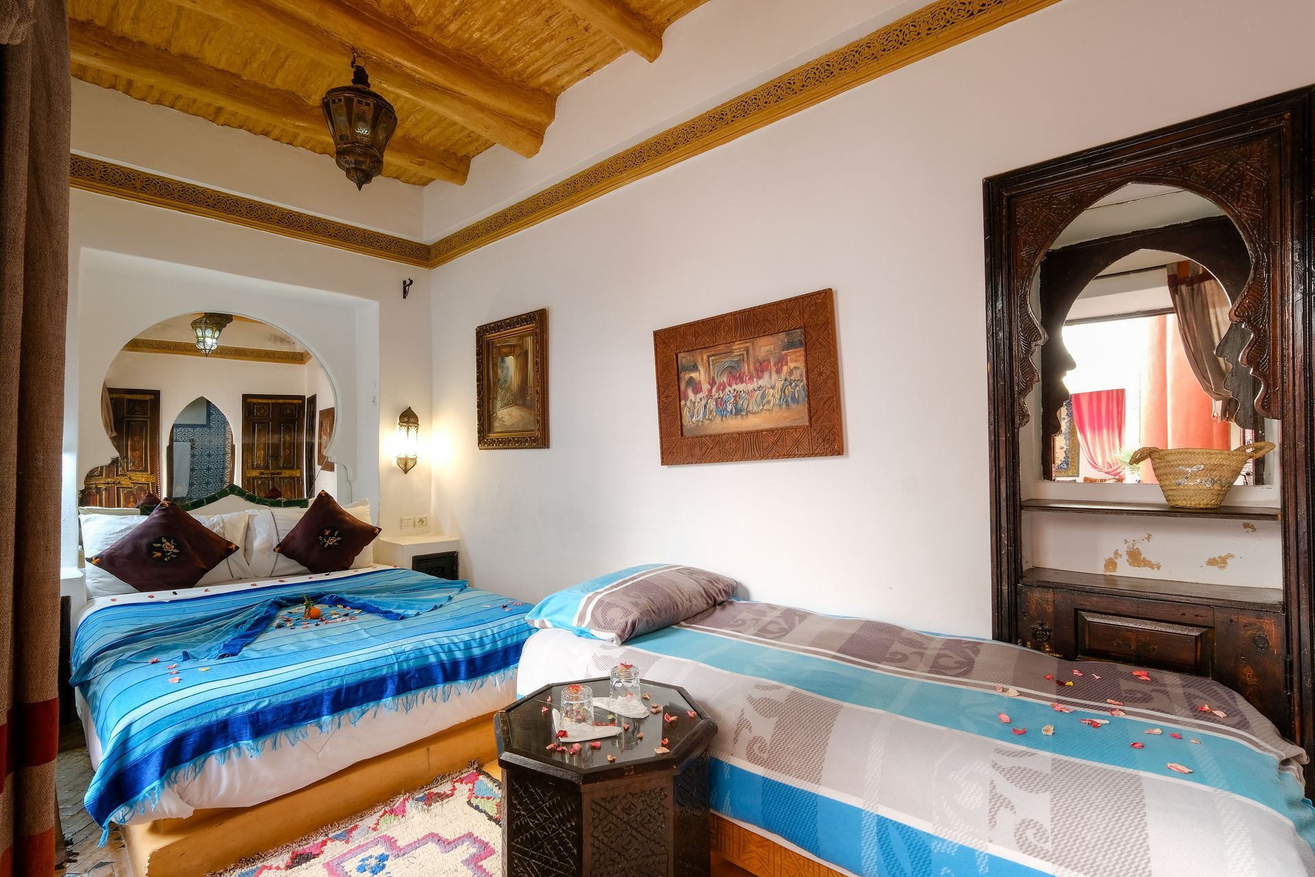 Bedroom in a Moroccan riad with two beds, ornate wooden accents, and colorful bedding.