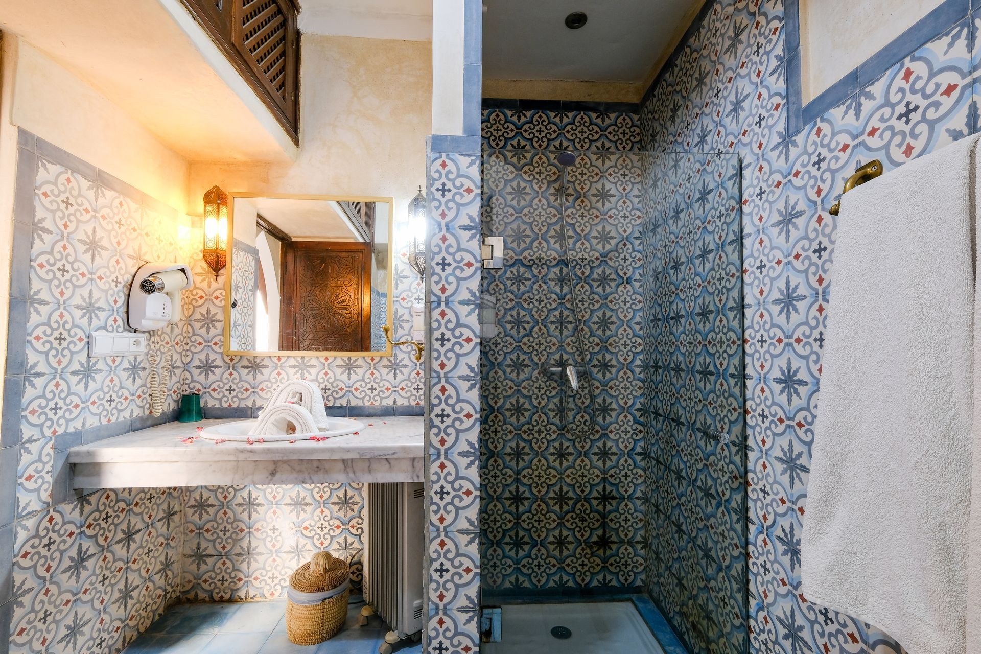 Bathroom with patterned tile walls and shower, white towels, and a sink.