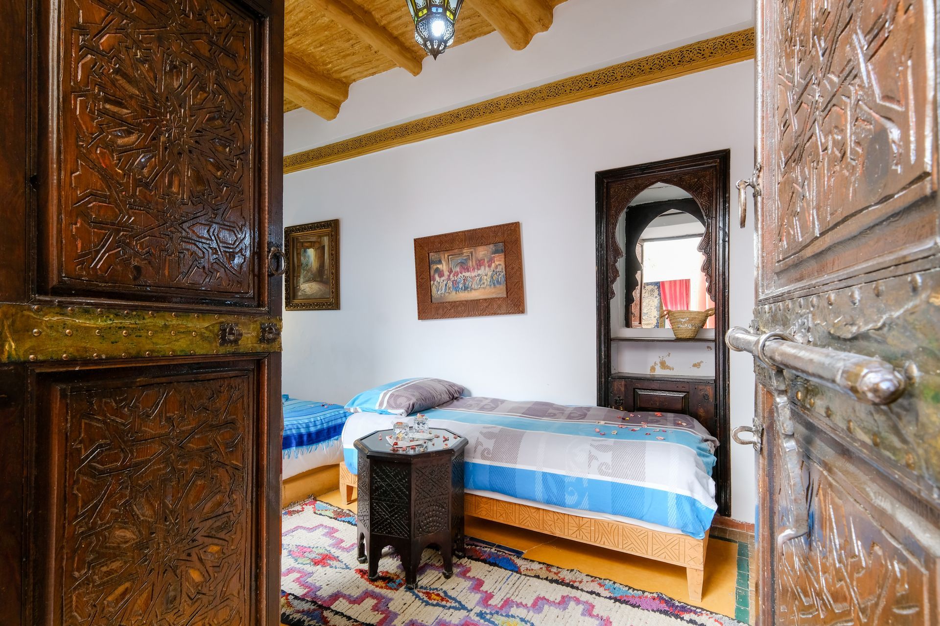 Bedroom interior with ornately carved wooden doors, two beds, and a patterned rug.