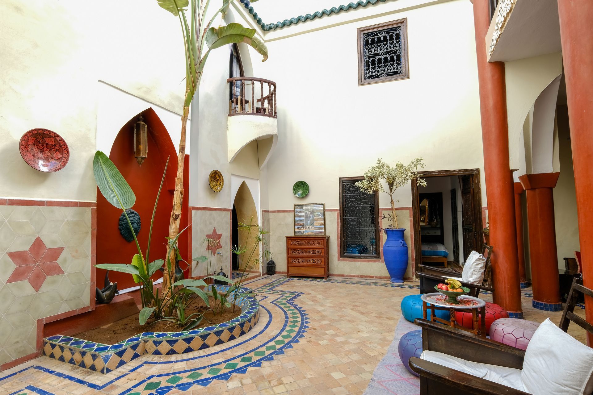 Courtyard with colorful tilework, red pillars, arched doorways, and plants.