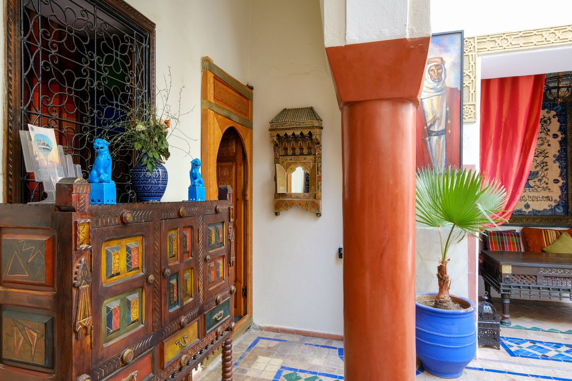 A Moroccan-style courtyard with an ornate cabinet, mirror, and column, with bright colors and plants.