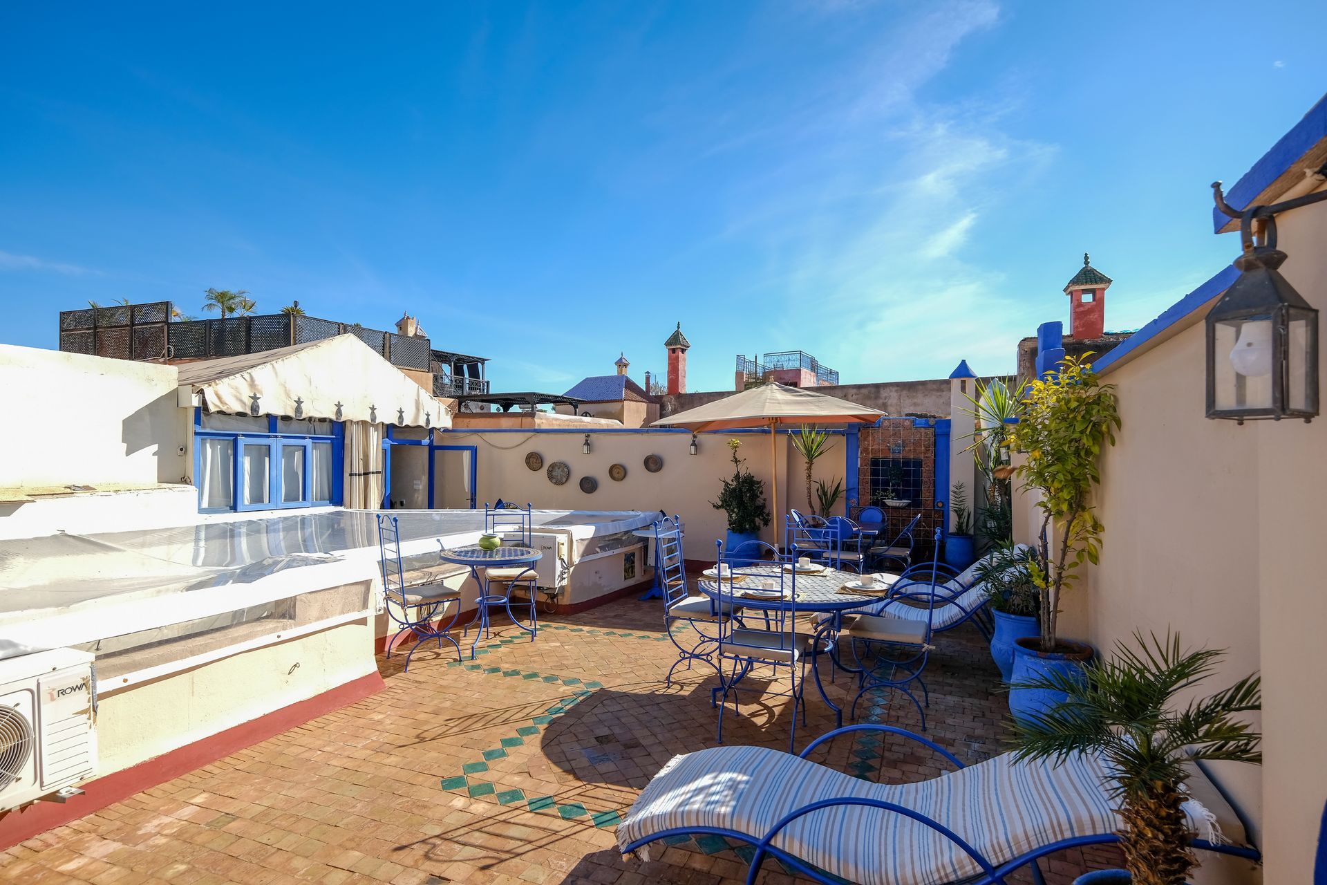Rooftop patio with blue accents, tables, chairs, and umbrella under a bright blue sky.