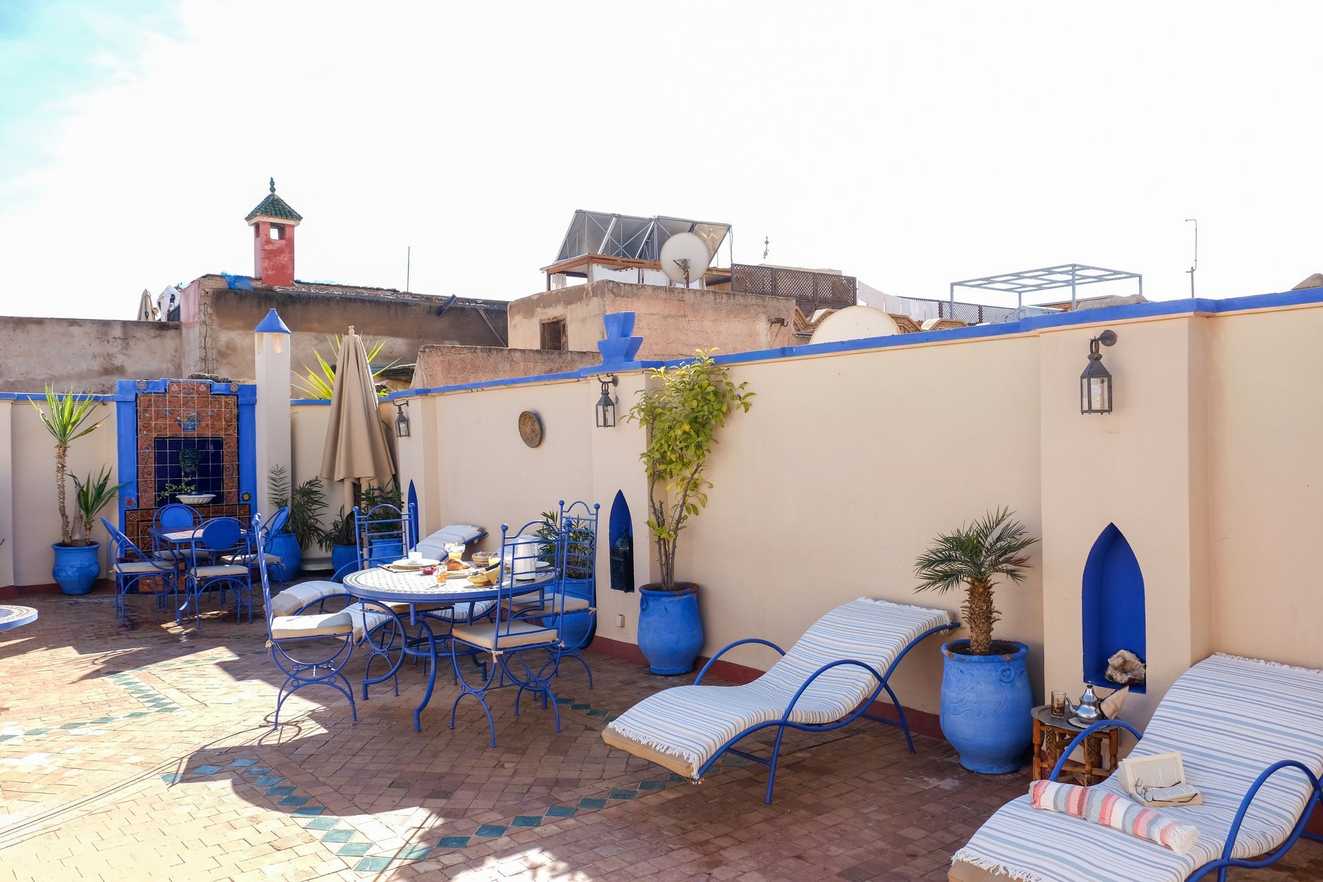 Rooftop patio with blue furniture, lounge chairs, and potted plants in Morocco.