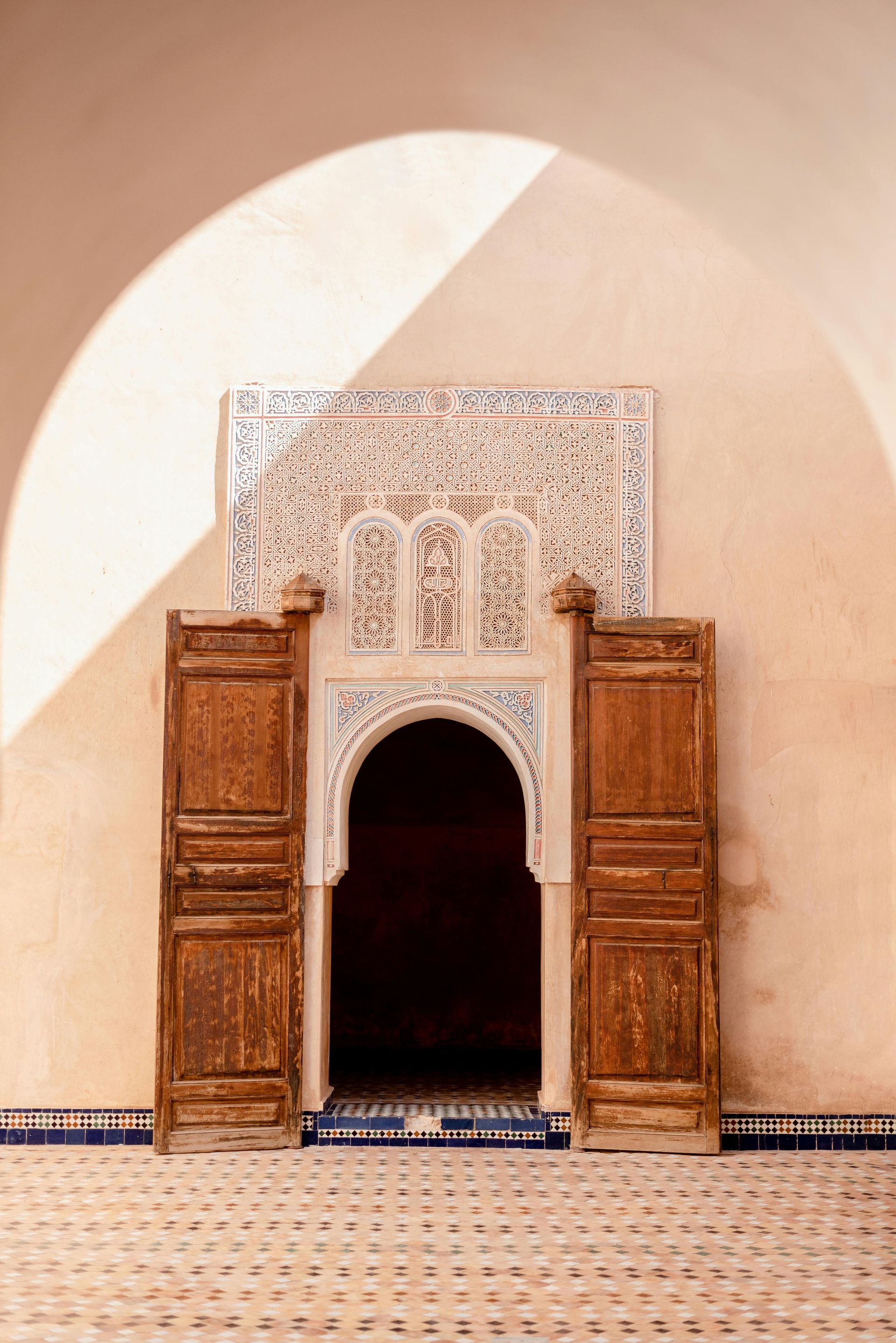 Ornate archway with weathered wooden doors in a light-filled courtyard, decorated with intricate tilework.