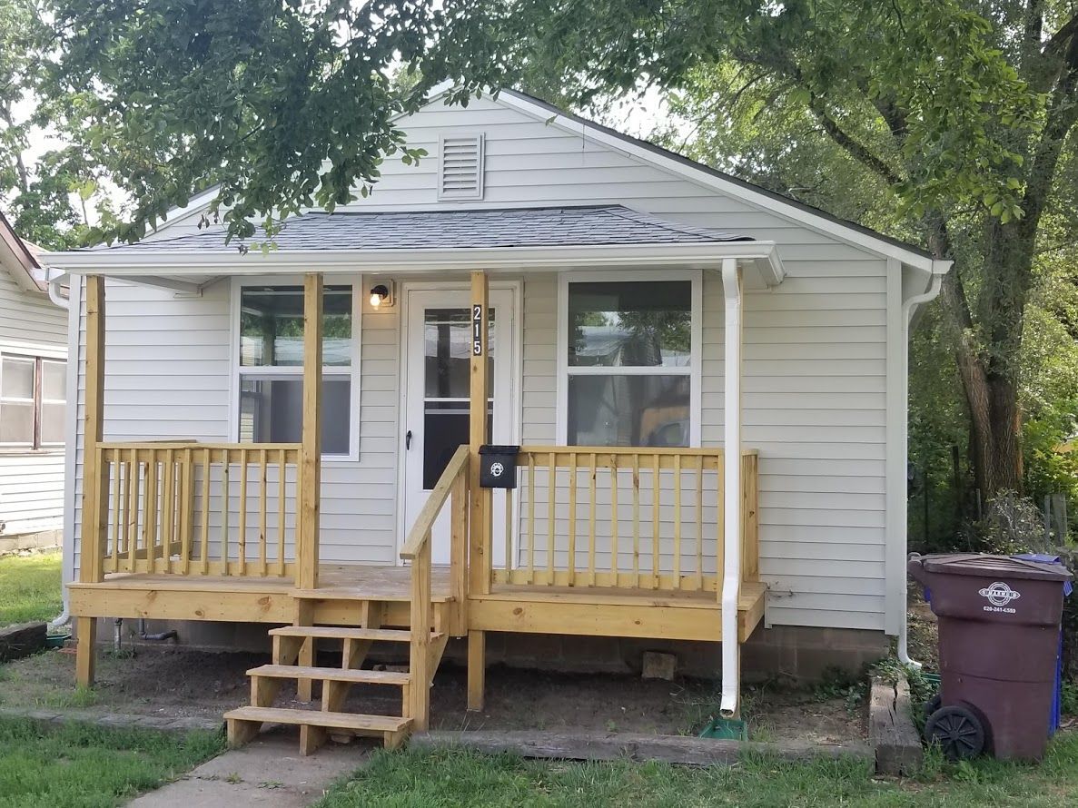 A small white house with a wooden porch and stairs.