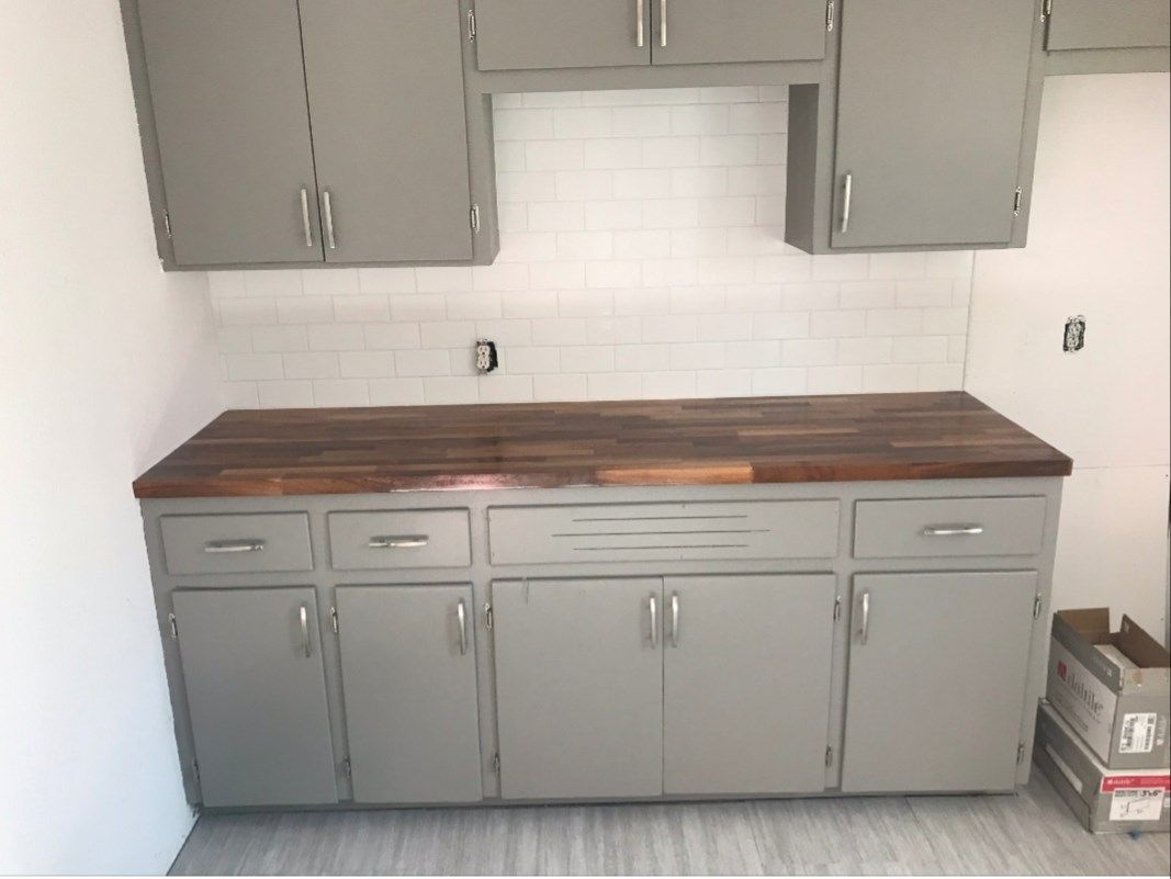 A kitchen with gray cabinets and a wooden counter top