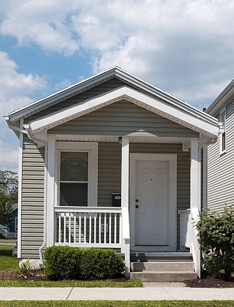 A small white house with a porch is sitting in the middle of a lush green field.