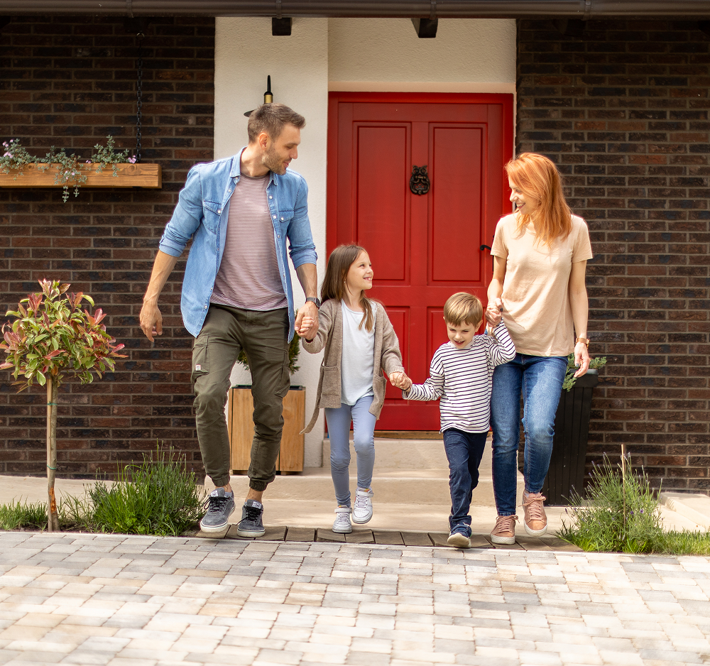 Family of four holding hands, exiting a home with red door.