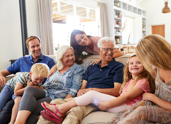 Family sitting on a couch, smiling. Grandparents, parents, and children in a living room.