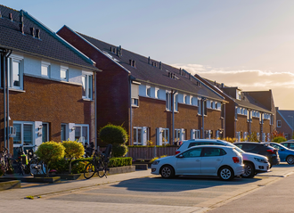 Row of brick townhouses with parked cars on a sunny day.