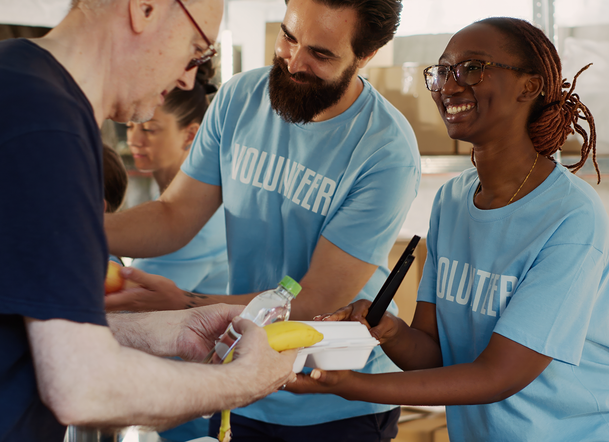 Volunteers in blue shirts distributing food and water. Smiling, multi-ethnic group in a warehouse.