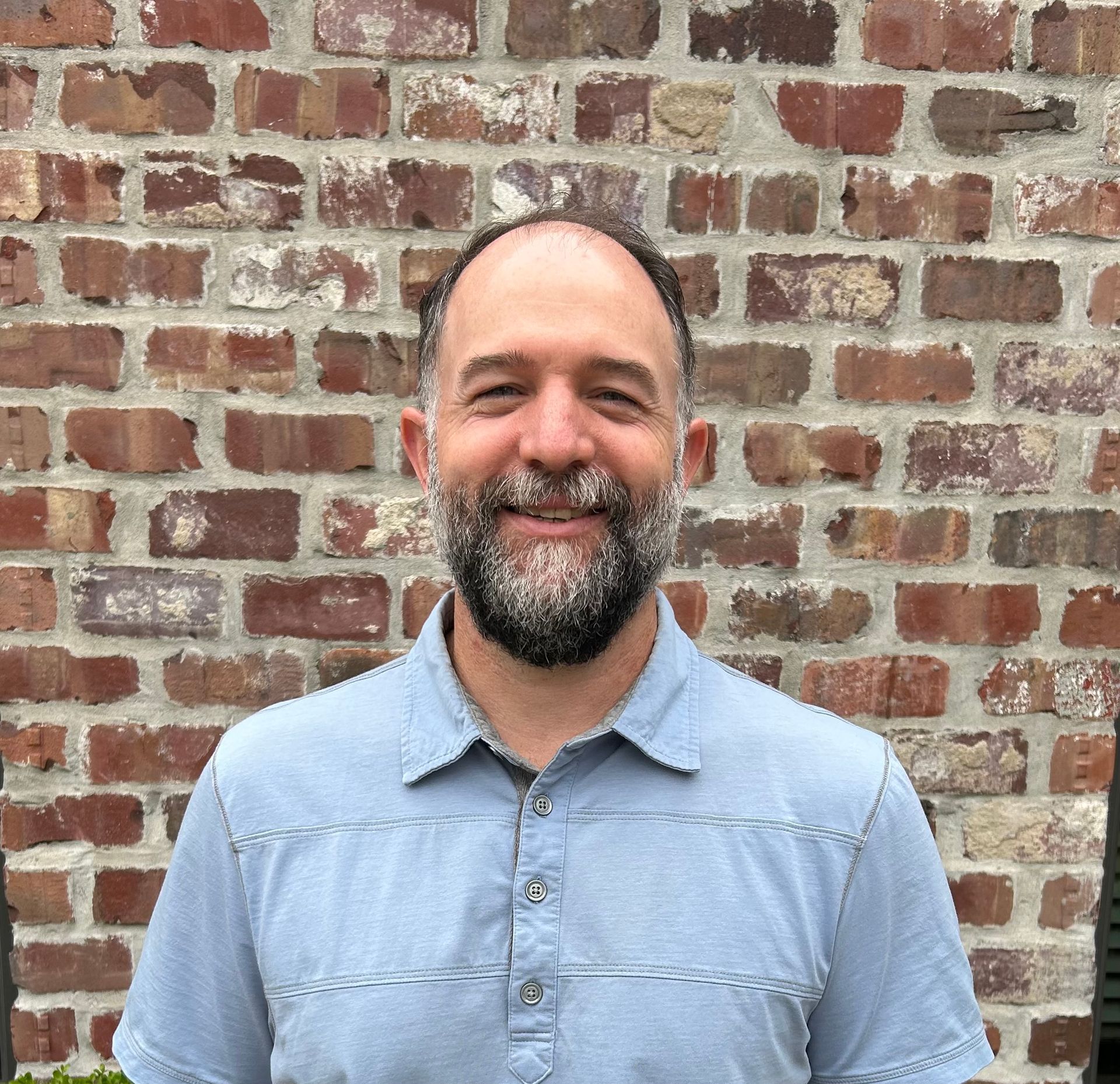 Man in suit smiling, light blue shirt, neutral background.