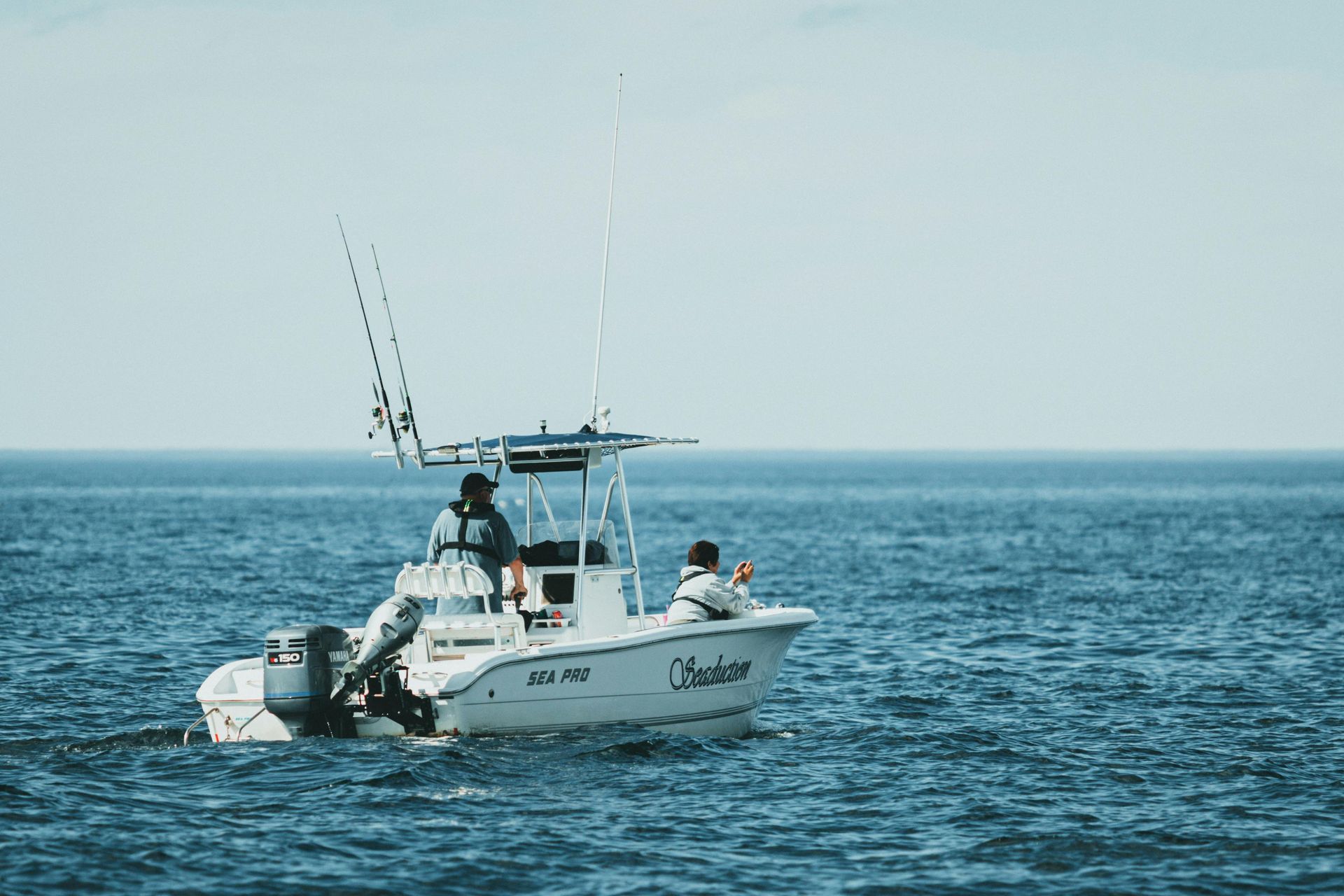 A fishing boat with two people on the water under a light blue sky.