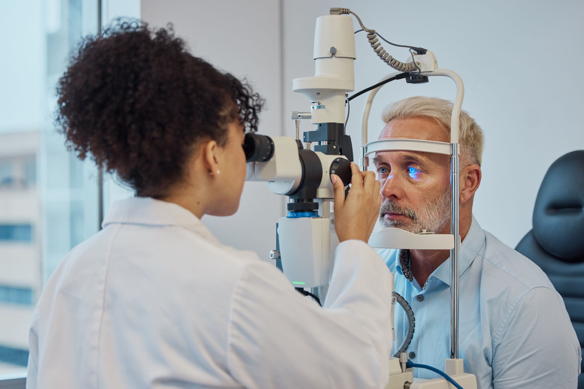 Optometrist examining a male patient's eyes with a slit lamp.